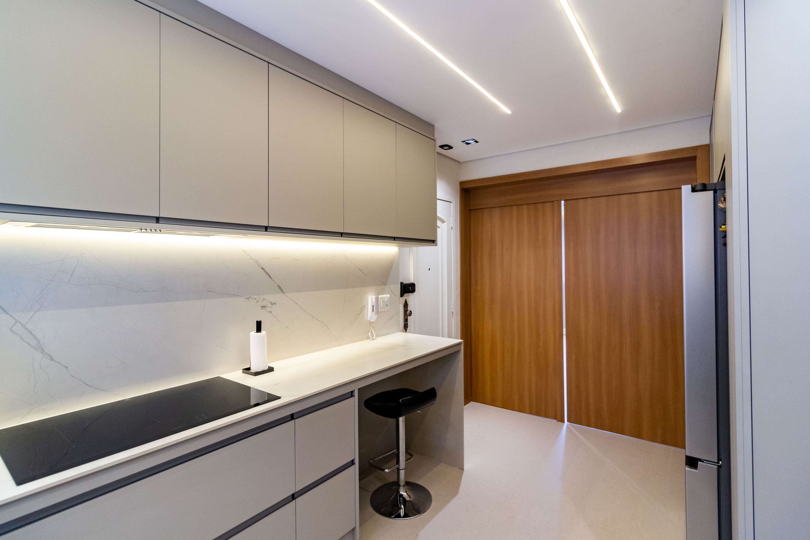 Ângulo oposto focado em uma bancada de refeições rápidas integrada aos armários, com uma banqueta preta e o painel de madeira da porta ao fundo.