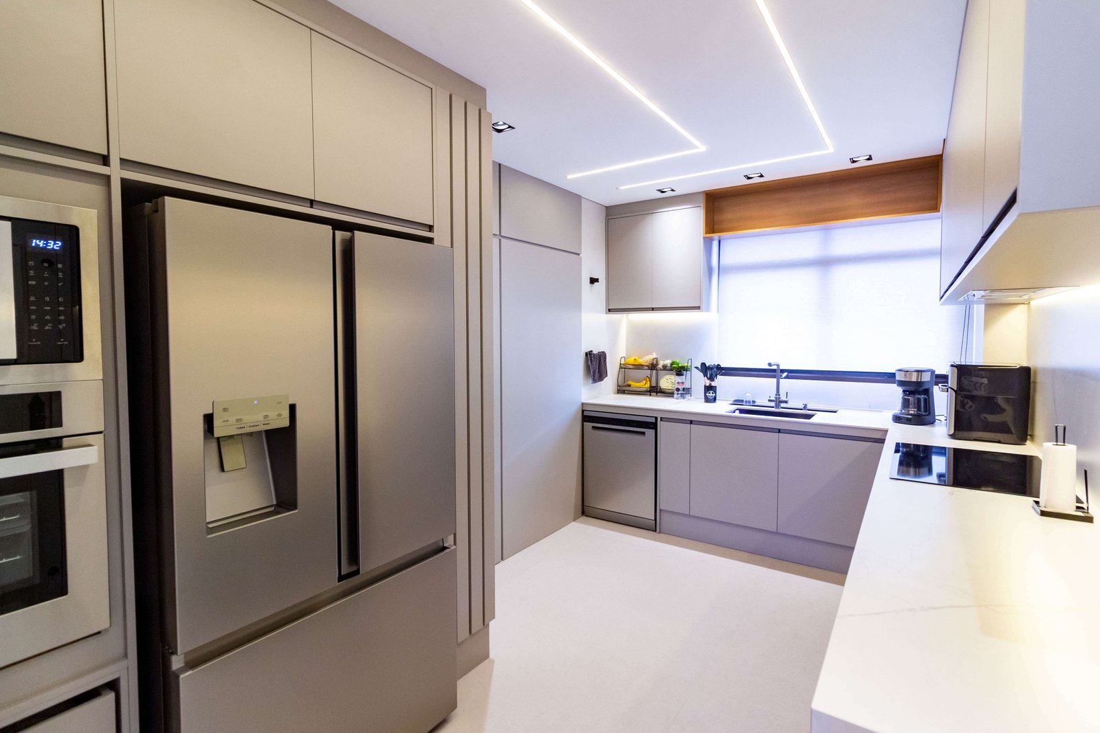 Outro ângulo da cozinha, vendo-se a geladeira à esquerda e a bancada da pia com lava-louças à direita. O piso é claro e reflete a luz natural.