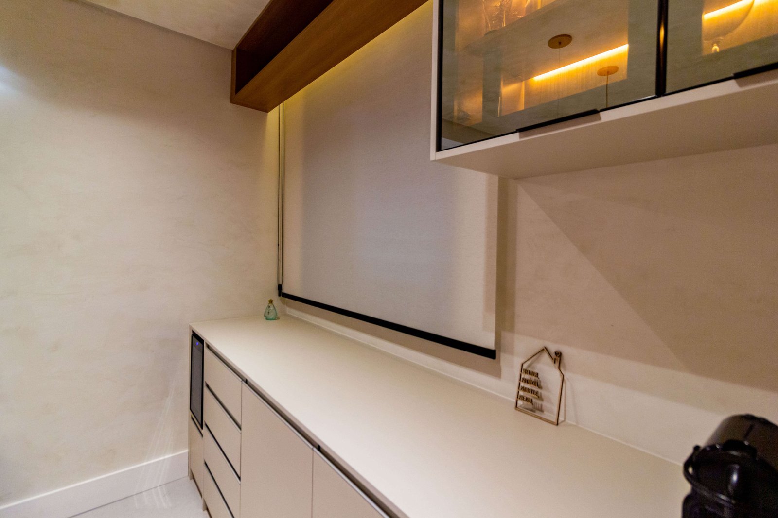 Close na bancada deste mesmo móvel, mostrando o acabamento fosco da marcenaria, objetos decorativos aramados e o detalhe de uma cristaleira aérea com vidro reflexivo no canto superior.