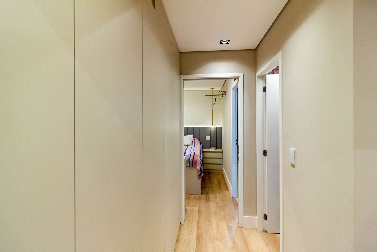 Um corredor de circulação aproveitado com armários embutidos do chão ao teto na cor bege, sem puxadores aparentes, criando um visual limpo e funcional.