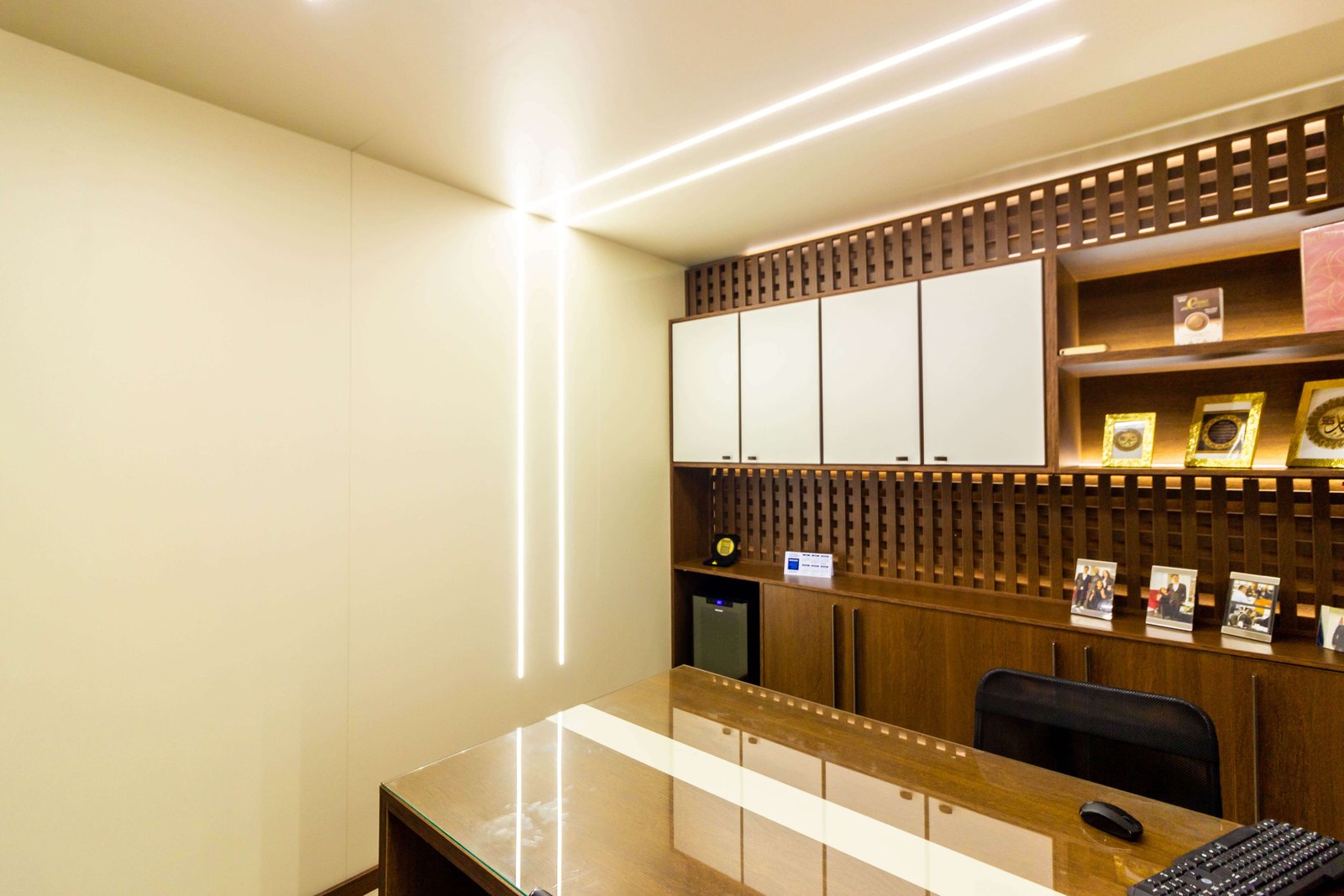 Escritório executivo de luxo com iluminação LED vertical na parede e armário planejado com fundo treliçado de madeira e portas brancas.