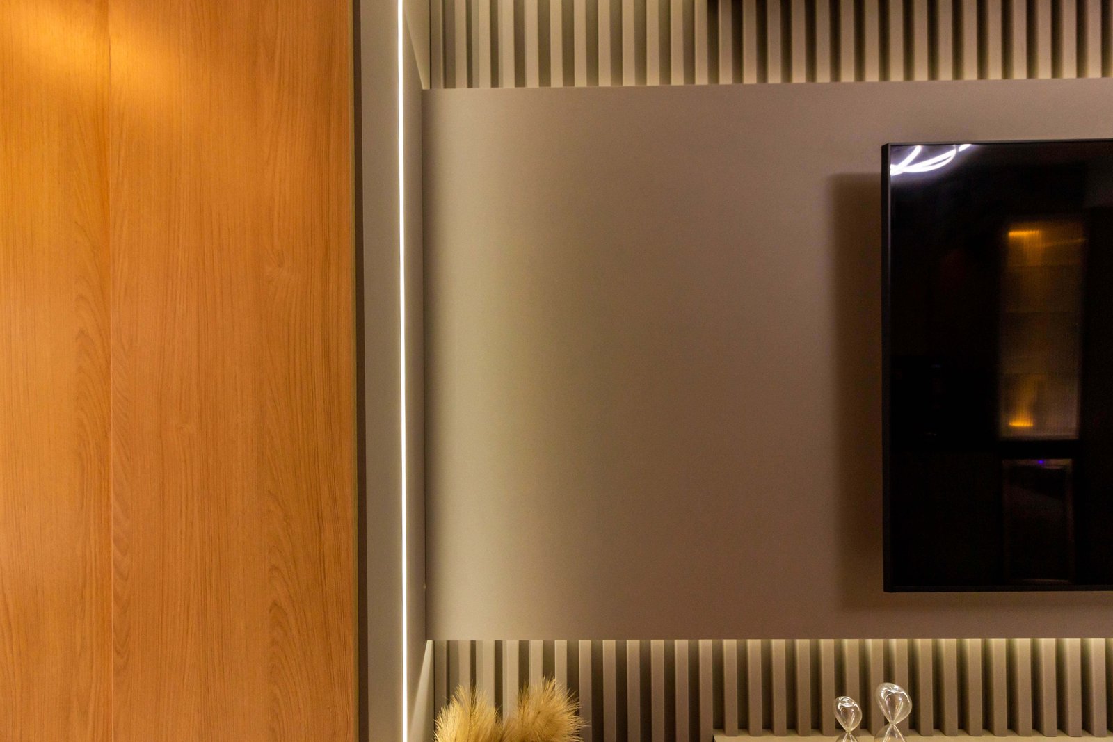 Close-up lateral (zoom) mostrando o acabamento perfeito do painel sobreposto ao ripado e o efeito da fita de LED embutida, criando uma luz indireta suave.