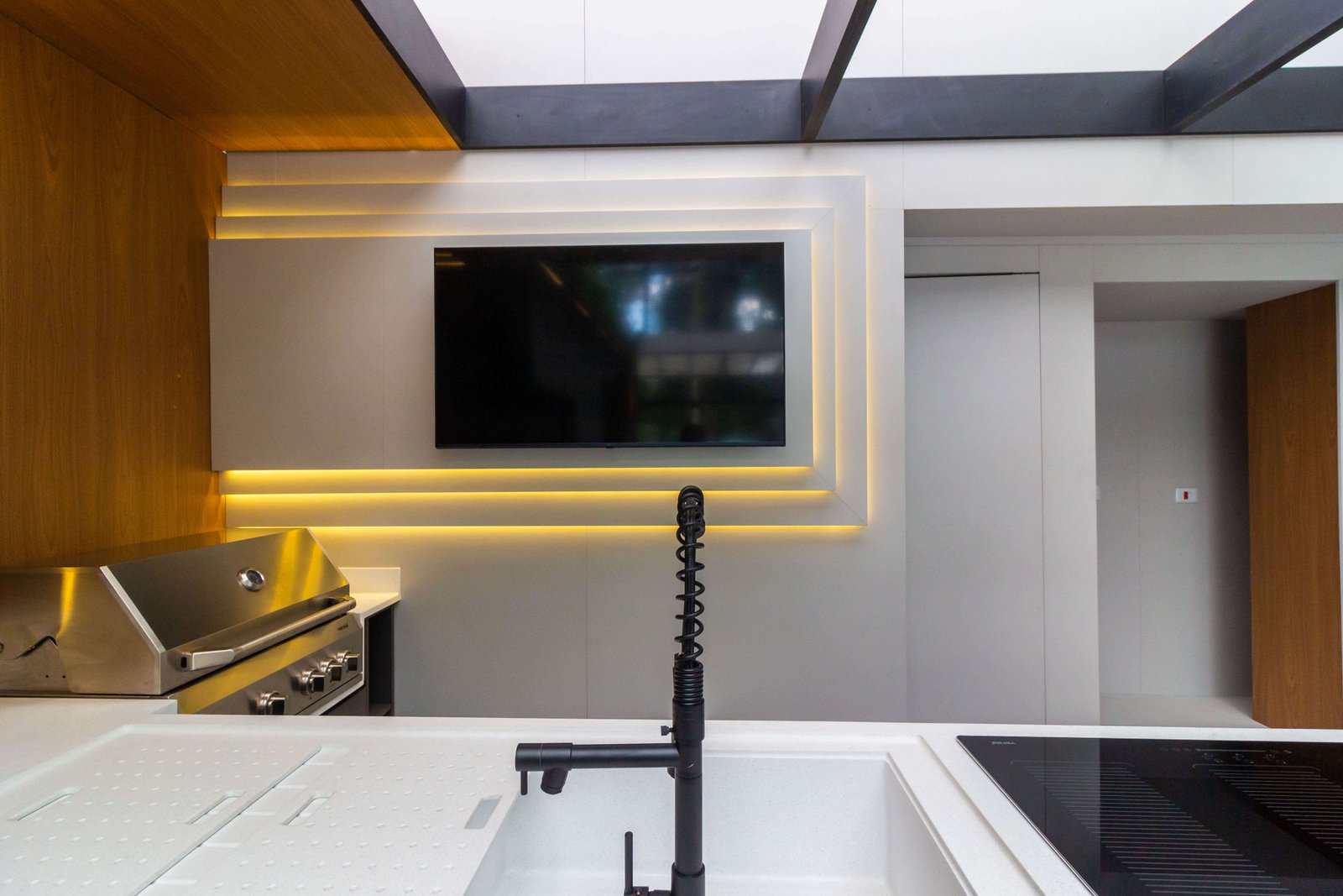 O painel da área gourmet (visto anteriormente) com design de molduras retangulares iluminadas por LED, posicionado acima da bancada da churrasqueira.