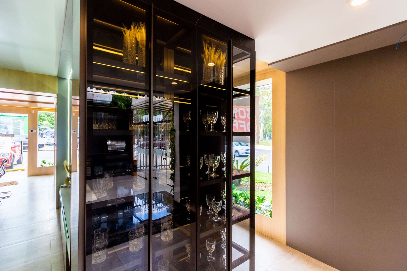 Cristaleira planejada de alto padrão com portas de vidro, perfil de alumínio preto e iluminação interna em LED, exibindo taças e decorações no showroom da Zogbi em São Paulo.
