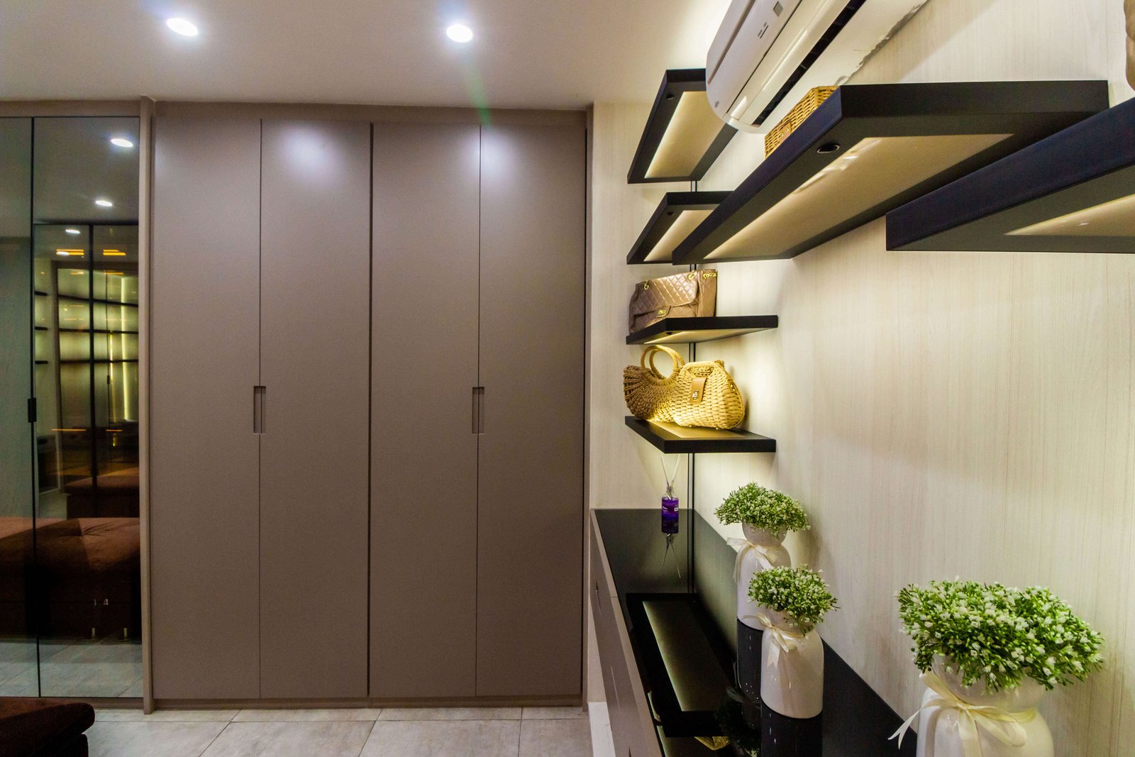 Closet planejado em tom neutro com portas de armário altas e nichos laterais abertos com iluminação LED para exposição de bolsas e acessórios, otimização de espaço em SP.