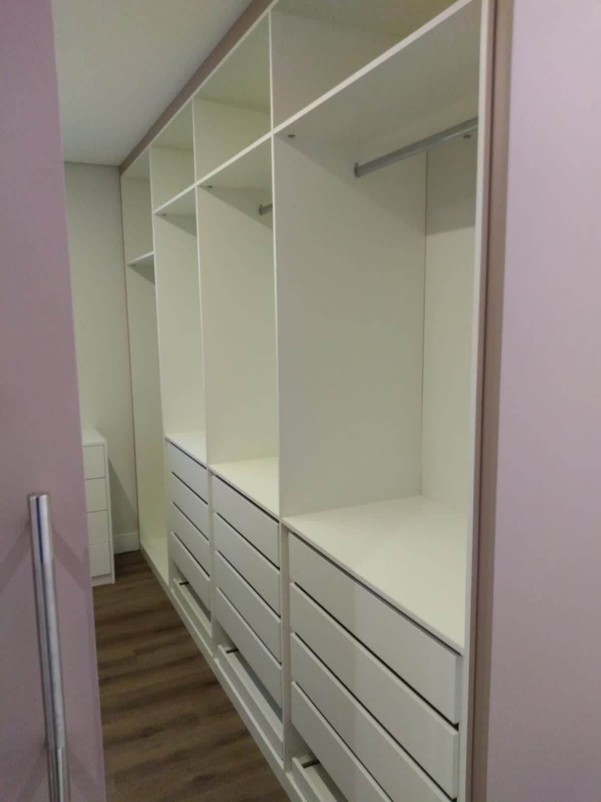 O interior de um closet ou guarda-roupa planejado branco e vazio, destacando a organização interna com nichos superiores, varões para cabides e gaveteiros na parte inferior.